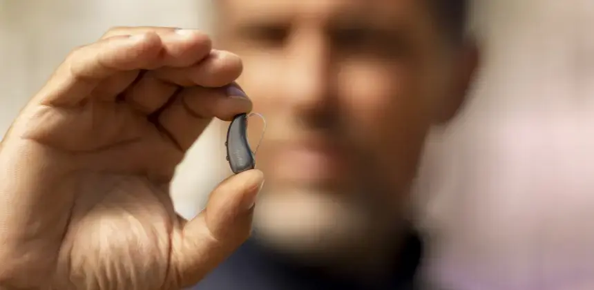 Hombre mostrando un audífono moderno con tecnología digital para mejora auditiva