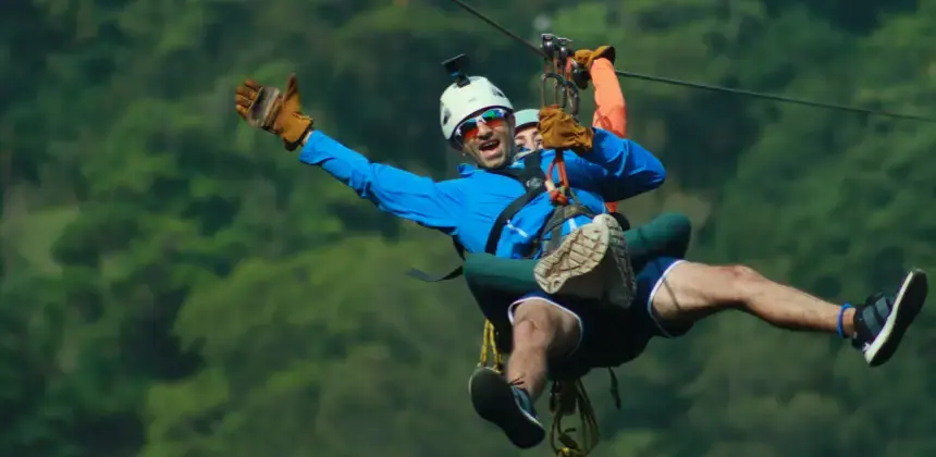 Hombre disfrutando un recorrido en canopy con equipo de seguridad y fondo de bosque verde