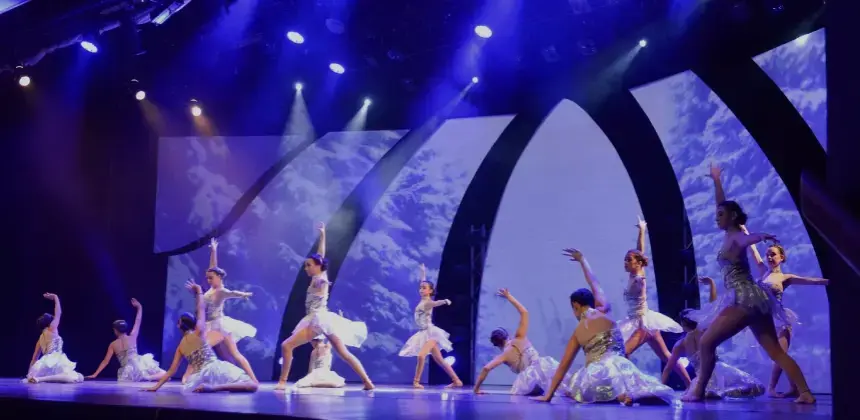 Grupo de bailarinas realizando una coreografía en un escenario iluminado con luces azules.