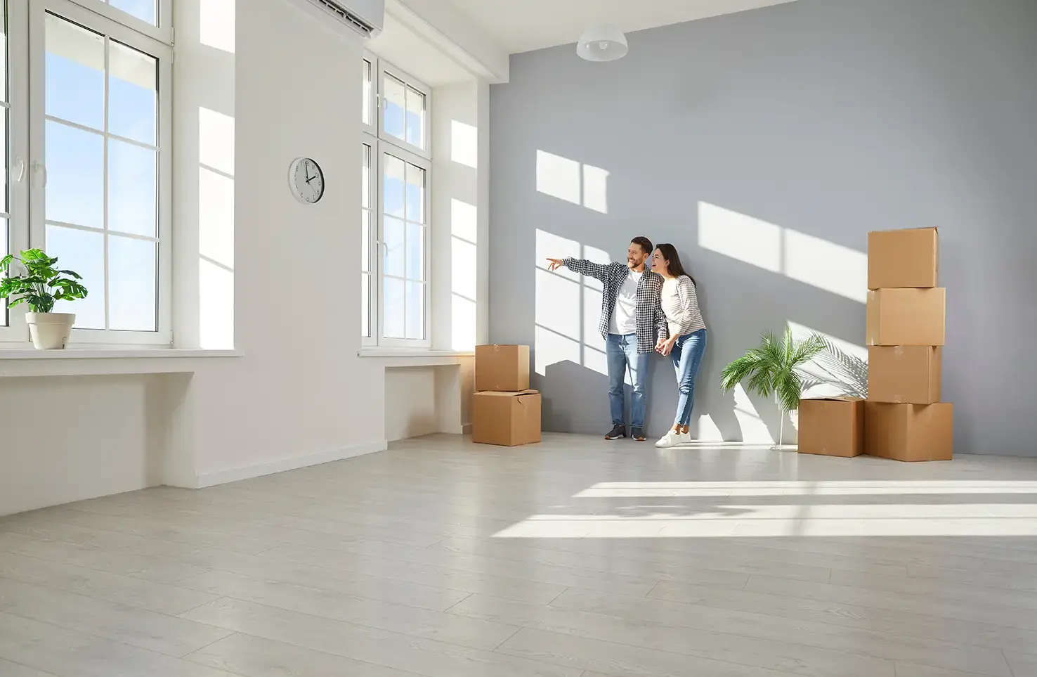 Pareja observando un espacio vacío con cajas de mudanza dentro de una habitación iluminada.