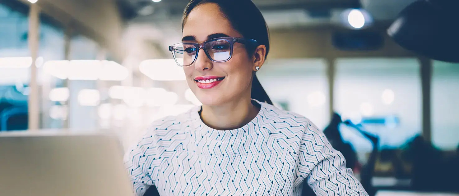 Mujer trabajando frente a una computadora portátil mientras toma notas en una libreta.