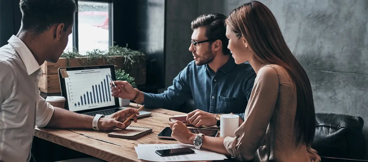 Tres personas analizando una gráfica en una computadora portátil durante una reunión de trabajo.