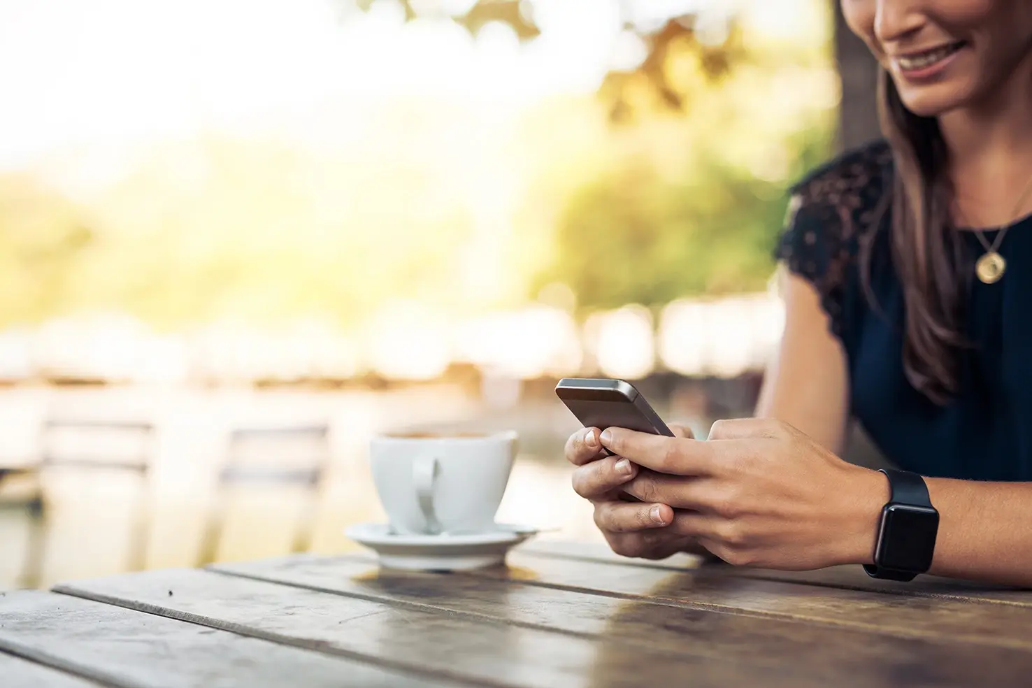 Persona usando su teléfono móvil en una mesa al aire libre junto a una taza de café.