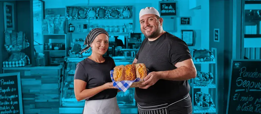 Panaderos sonrientes mostrando una bandeja de pan recién horneado en su panadería.
