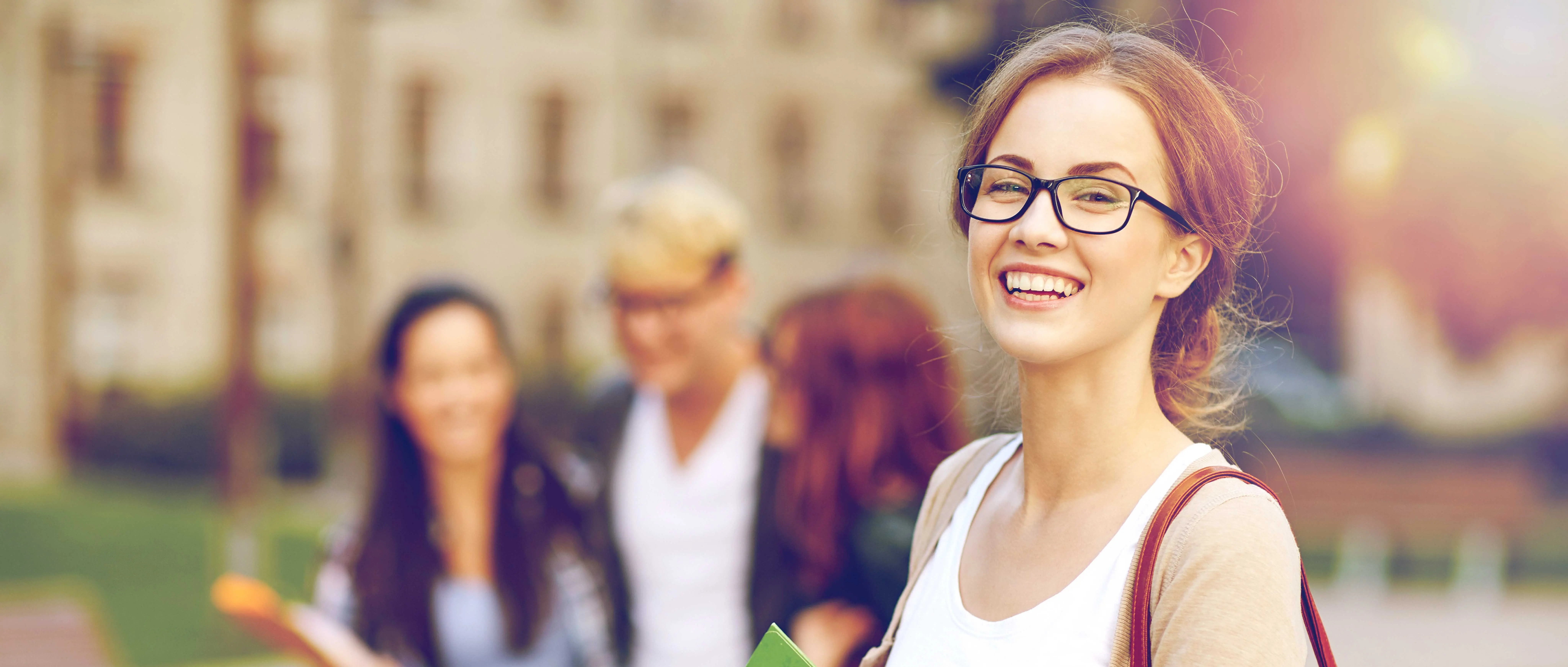 Joven con gafas sosteniendo una carpeta verde, sonriendo a cámara, con tres personas desenfocadas en el fondo.