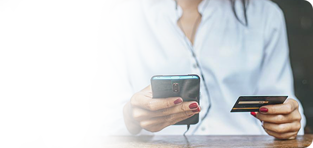 Mujer realizando una compra en línea con su tarjeta en la mano y un celular en la otra.