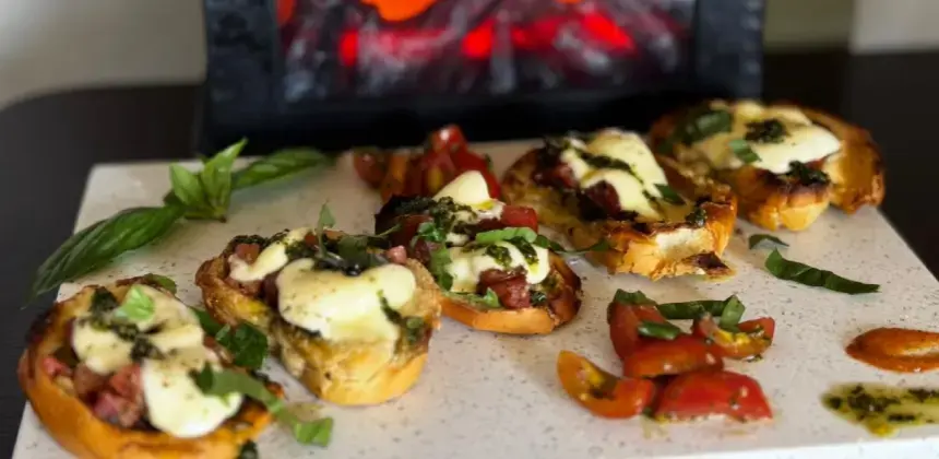 Bruschettas con queso derretido, tomates y albahaca servidas sobre una base de piedra.