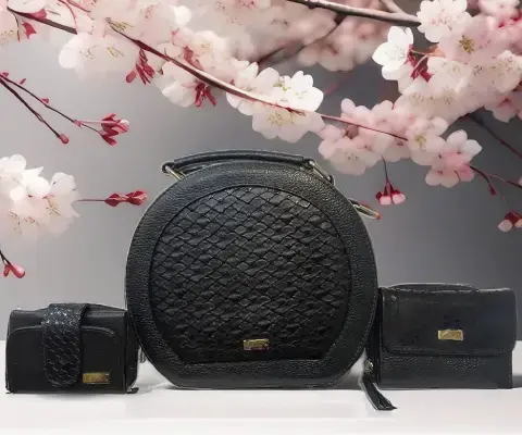 Carteras negras de diseño elegante exhibidas frente a fondo floral con ramas de cerezo