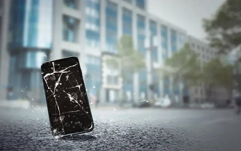 Teléfono móvil con la pantalla completamente rota tras caer sobre el pavimento de una calle urbana