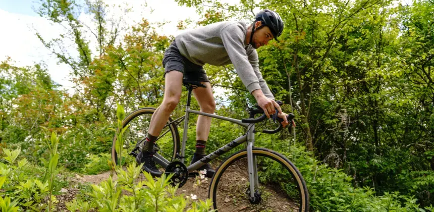 Ciclista con casco montando bicicleta de montaña en sendero rodeado de vegetación