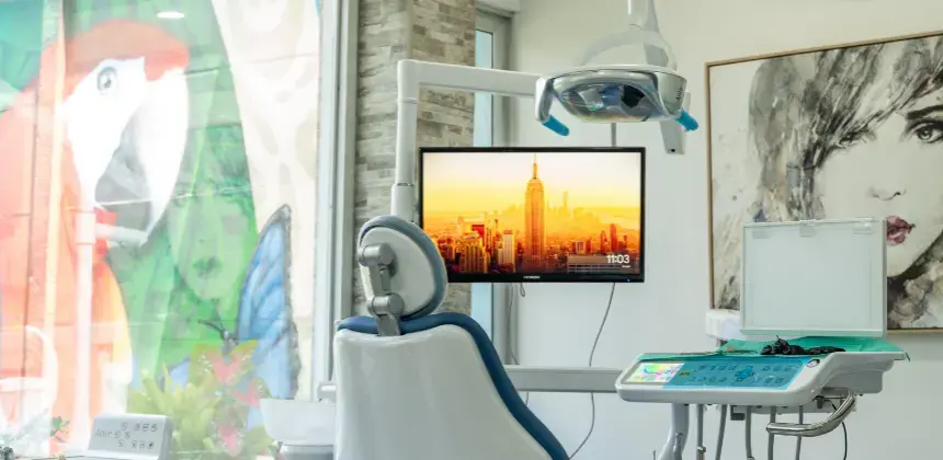 Consultorio dental moderno con sillón odontológico y pantalla encendida frente a una ventana decorada.
