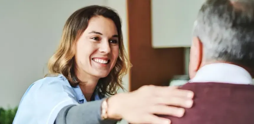 Cuidadora sonriendo mientras brinda apoyo a una persona mayor en entorno hogareño