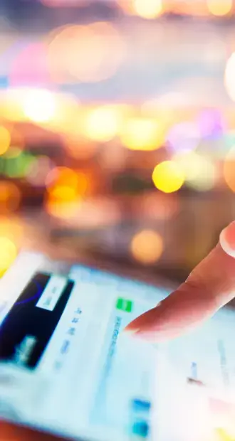 Dedo tocando la pantalla de un dispositivo móvil con una interfaz borrosa y luces de fondo desenfocadas, simbolizando interacción digital en un entorno dinámico.