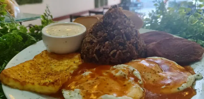 Plato de desayuno con arroz y frijoles, huevos en salsa, queso frito, tortillas y taza pequeña de salsa