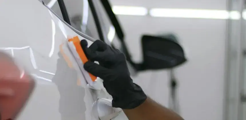 Persona con guantes negros aplicando recubrimiento sobre carro blanco en taller automotriz