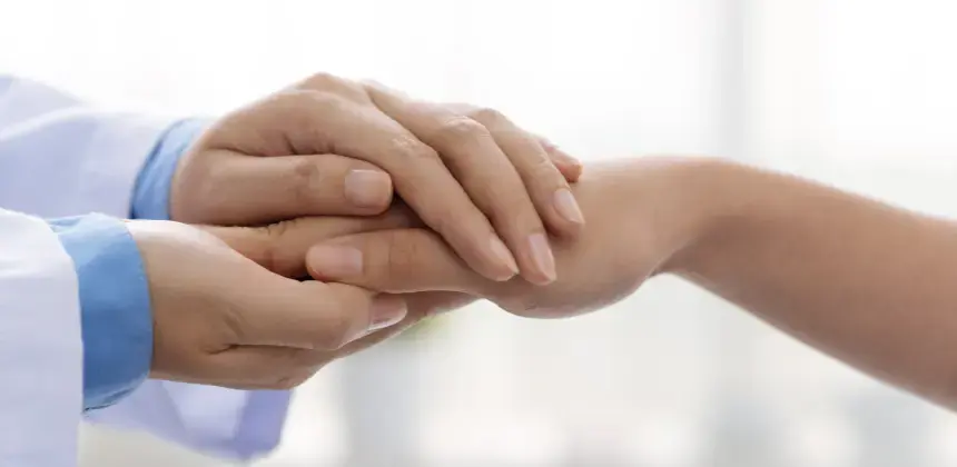 Médico sostiene la mano de un paciente en gesto de apoyo y confianza durante la consulta