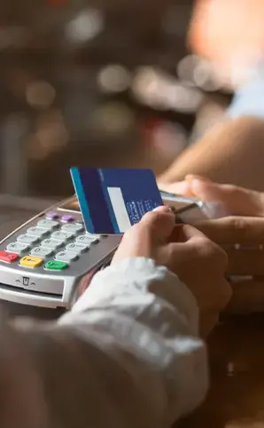 Persona realizando un pago en un datáfono con una tarjeta de crédito o débito en un entorno comercial.