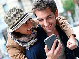 Pareja feliz riendo mientras mira un celular en una calle urbana