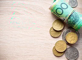 Billetes enrollados y monedas sobre una superficie de madera clara.