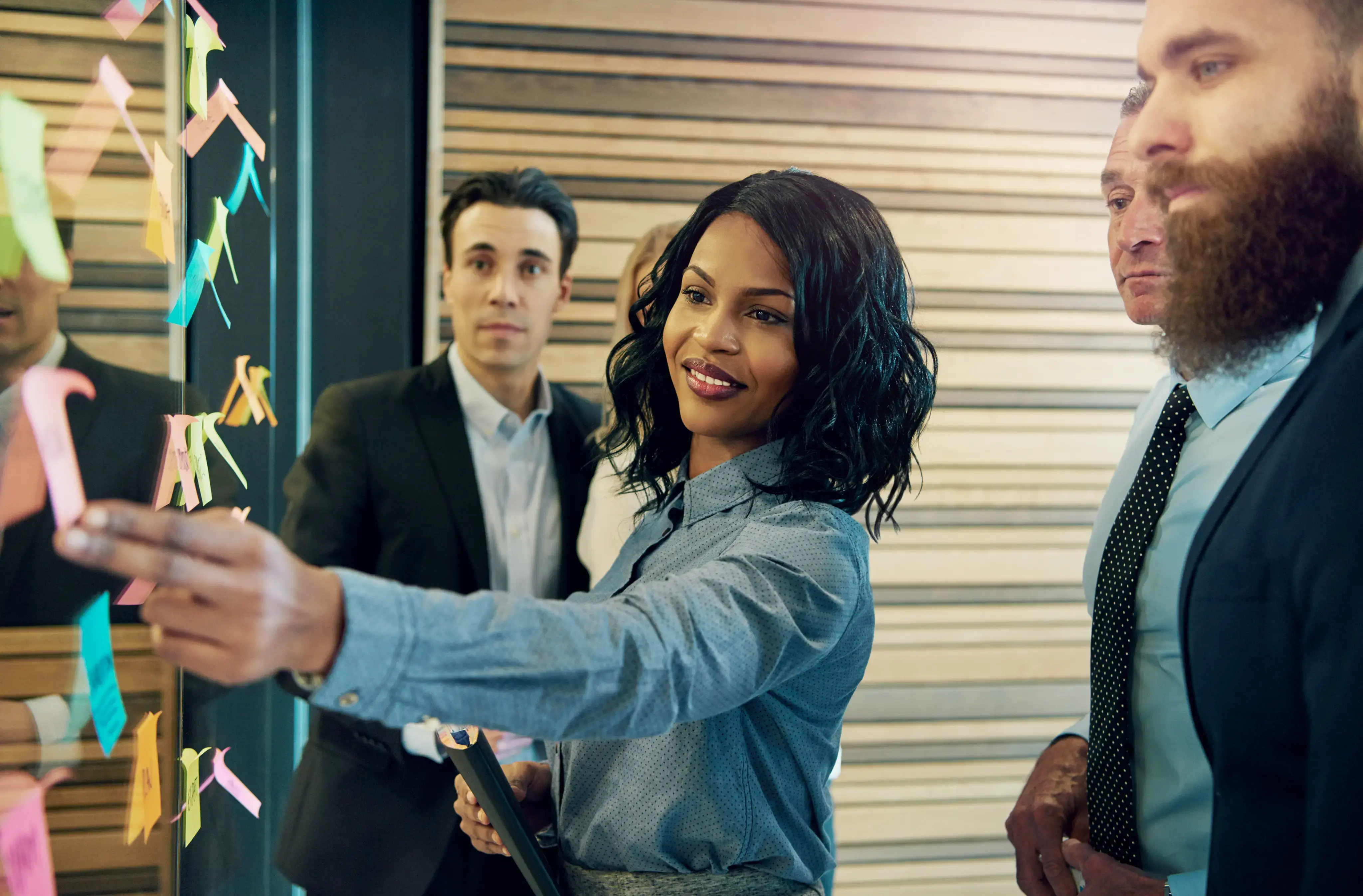 Equipo de trabajo frente a un tablero de notas adhesivas mientras una mujer señala una de las tarjetas.