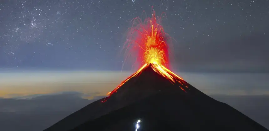 Erupción nocturna de volcán con lava incandescente y cielo estrellado en el fondo