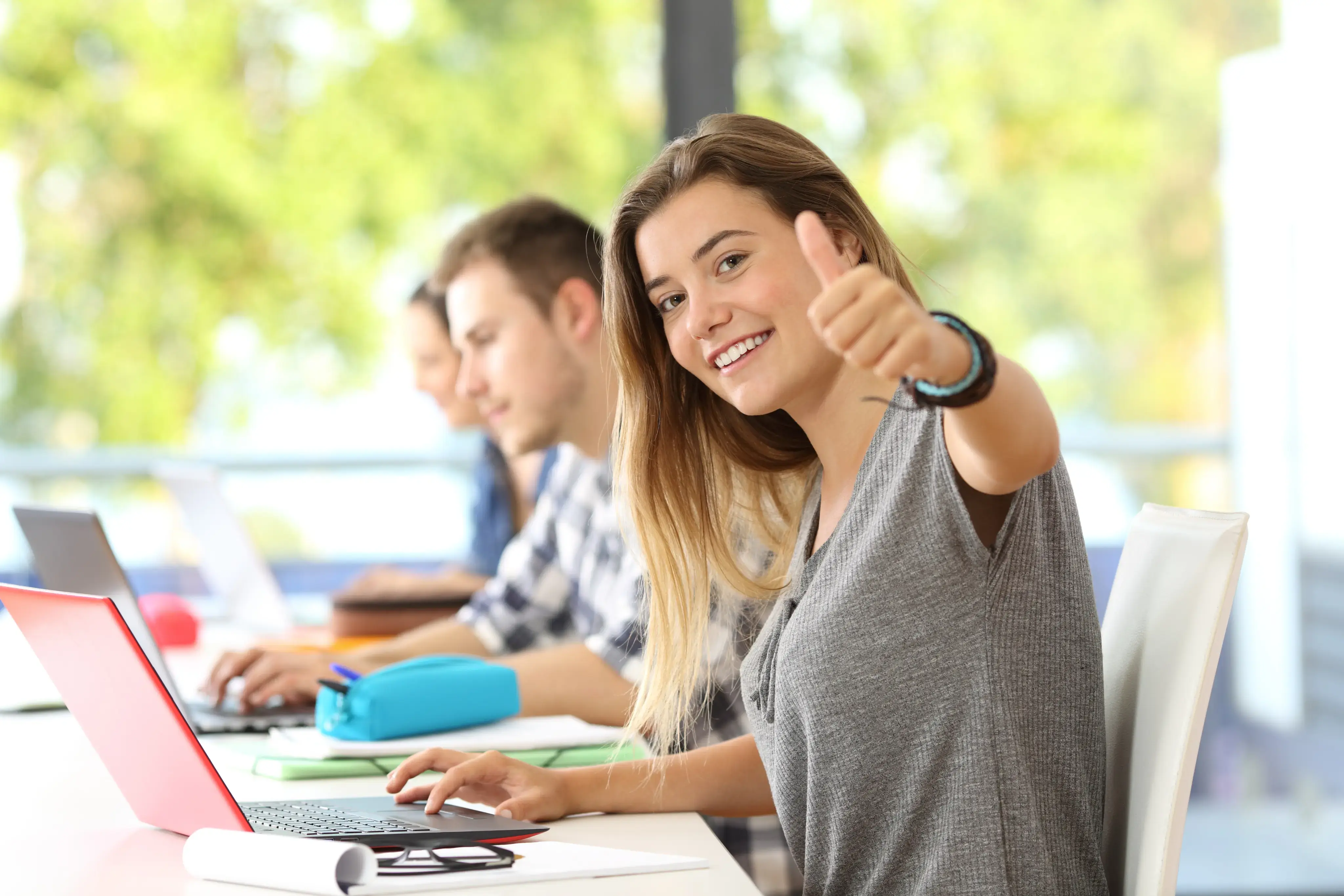 Estudiante sonriendo y levantando el pulgar mientras usa una computadora portátil.