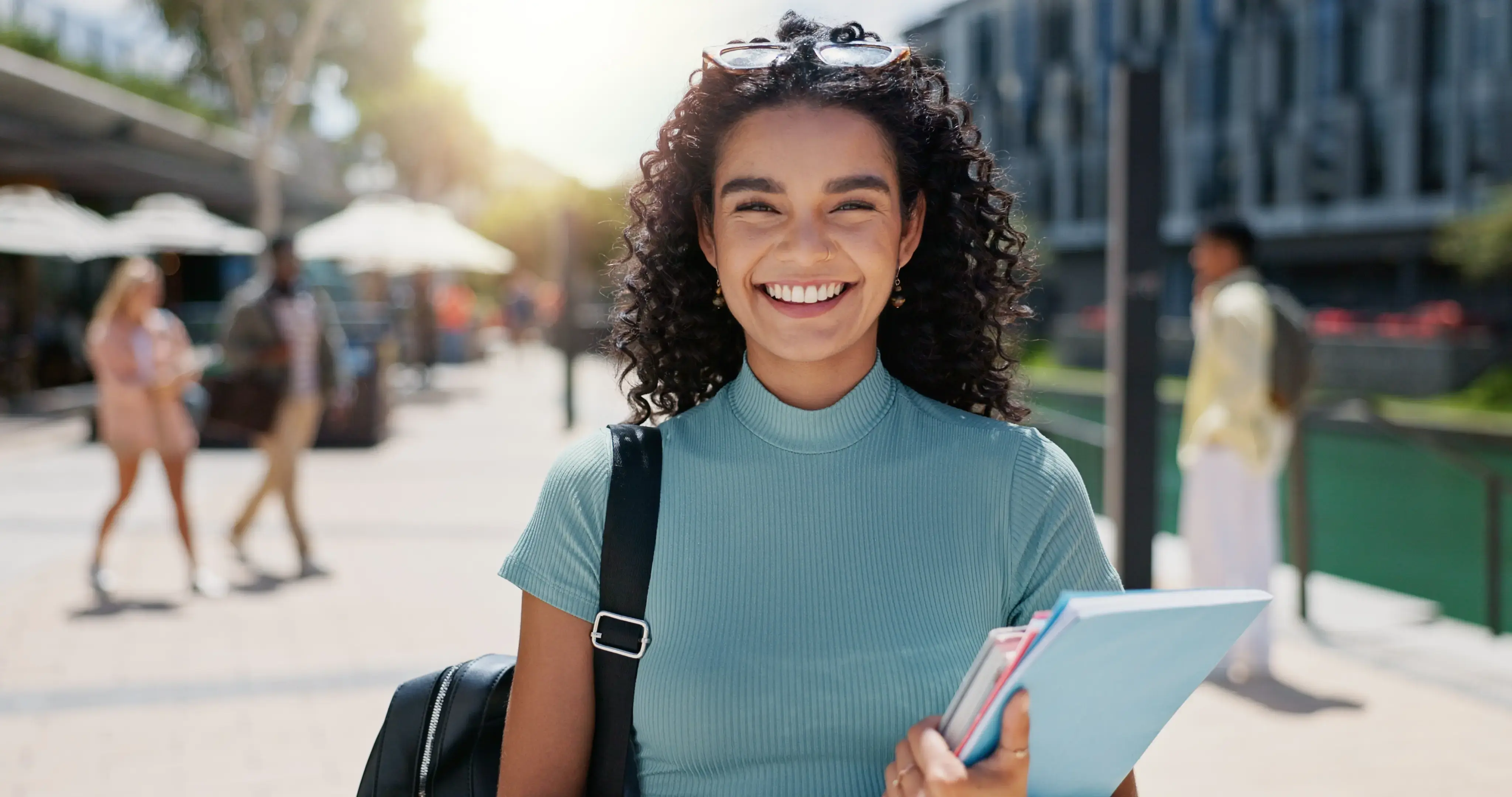 Estudiante joven sonriendo al aire libre con cuadernos en la mano.