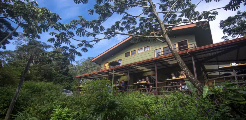 Fachada del Cala Lodge en Monteverde rodeada de vegetación con terraza y huéspedes desayunando