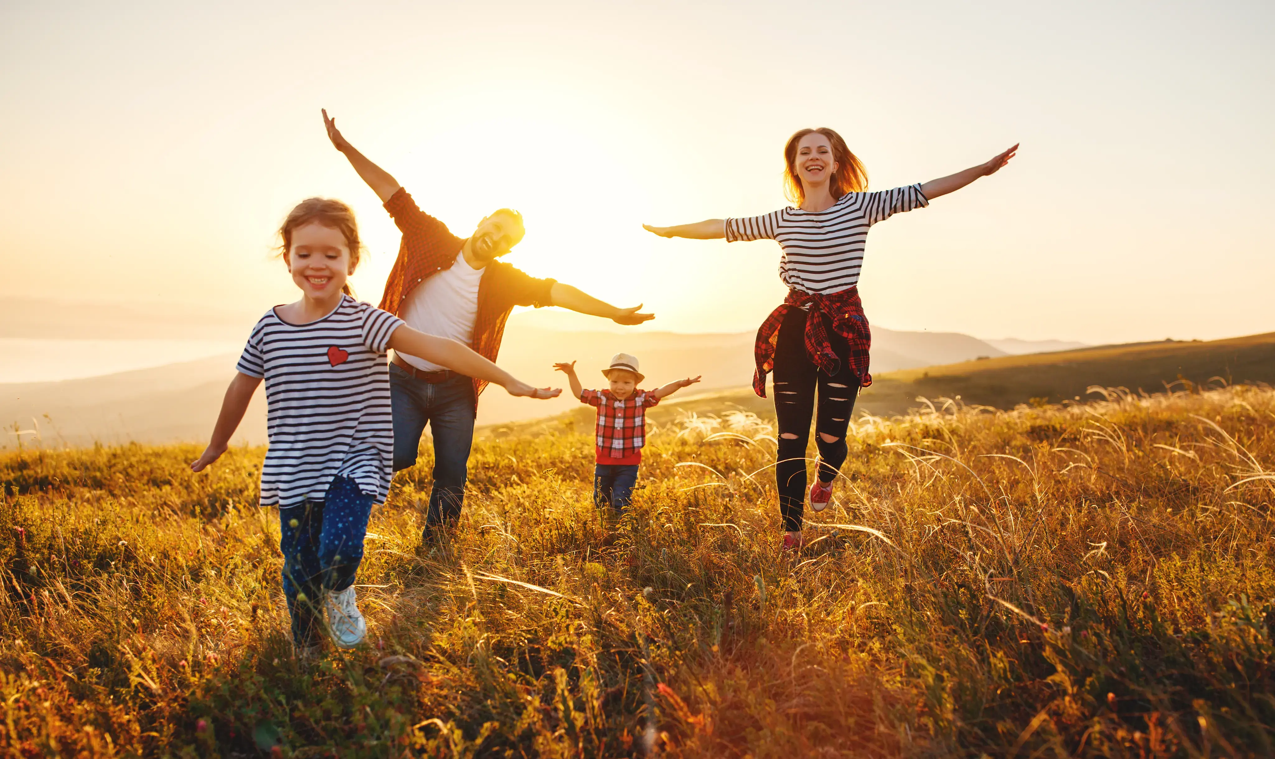 Familia corriendo y extendiendo los brazos en un campo iluminado por el sol.