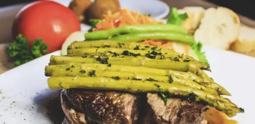 Filete de carne con espárragos y guarnición de vegetales servido en plato de restaurante