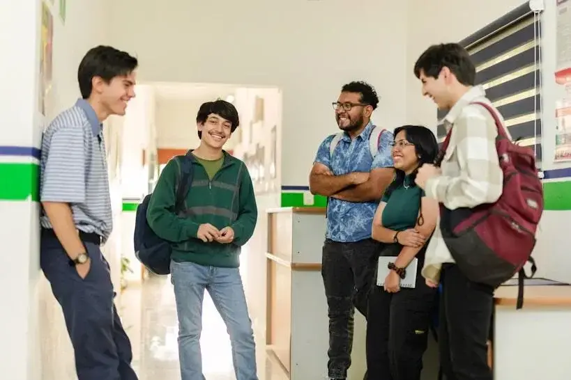 Grupo de estudiantes conversando y sonriendo en un pasillo escolar.