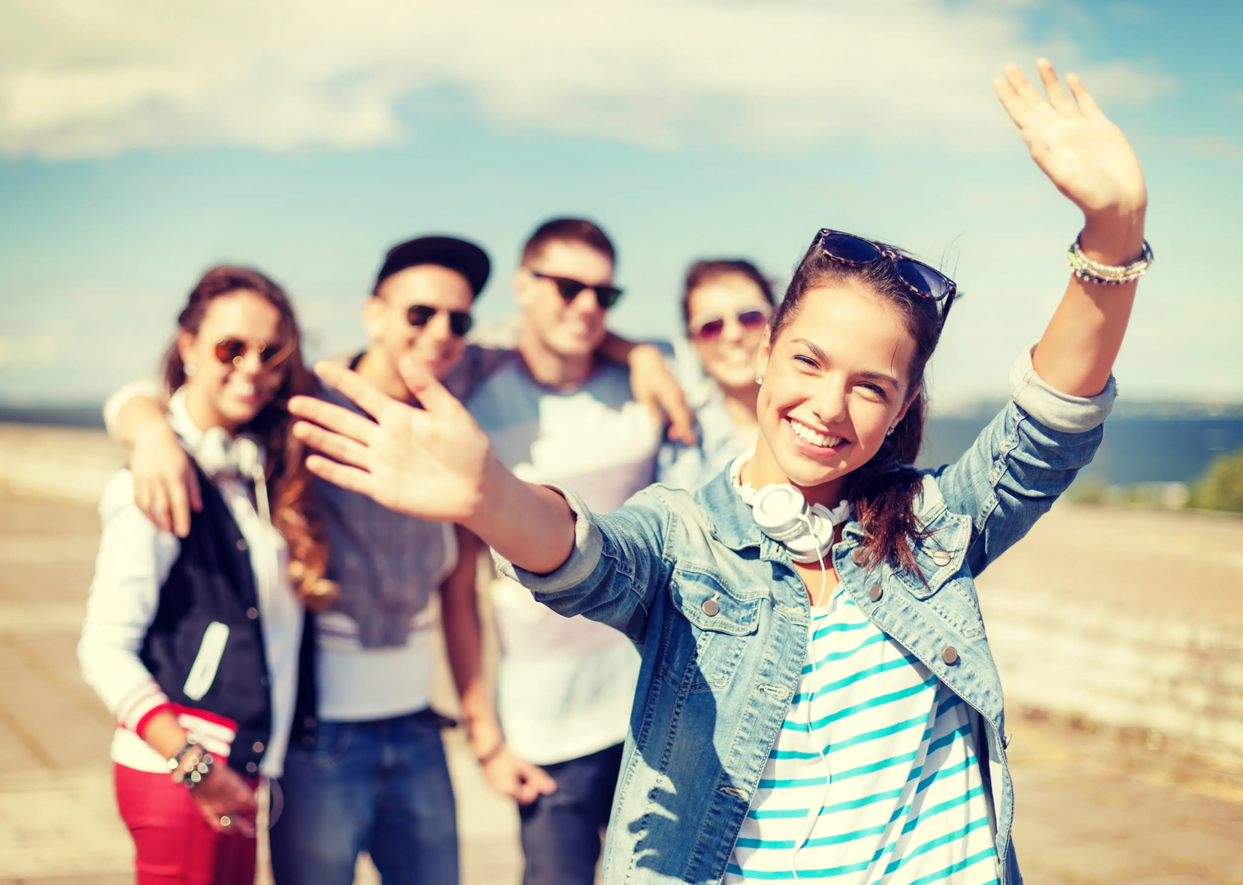 Grupo de jóvenes al aire libre con una chica al frente sonriendo y levantando los brazos.