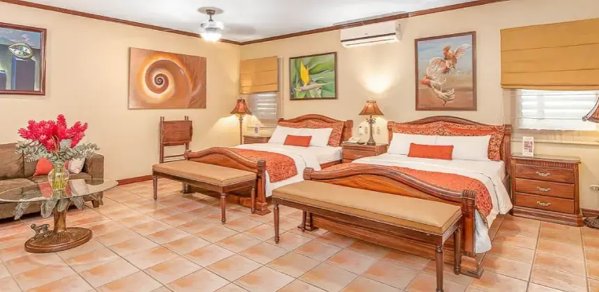 Habitación amplia con dos camas matrimoniales, muebles de madera, cuadros decorativos y lámparas cálidas en el Hotel Casa Roland San José