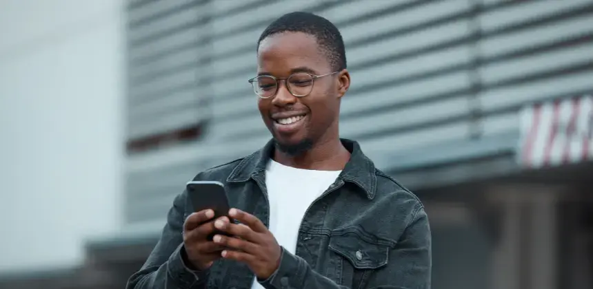 Hombre joven sonriendo mientras usa su teléfono móvil en la calle
