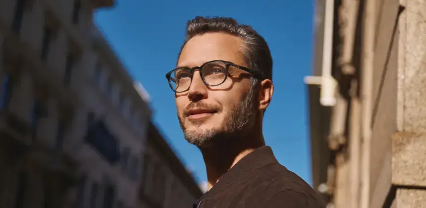 Hombre con gafas mirando hacia arriba bajo la luz del sol en una calle urbana