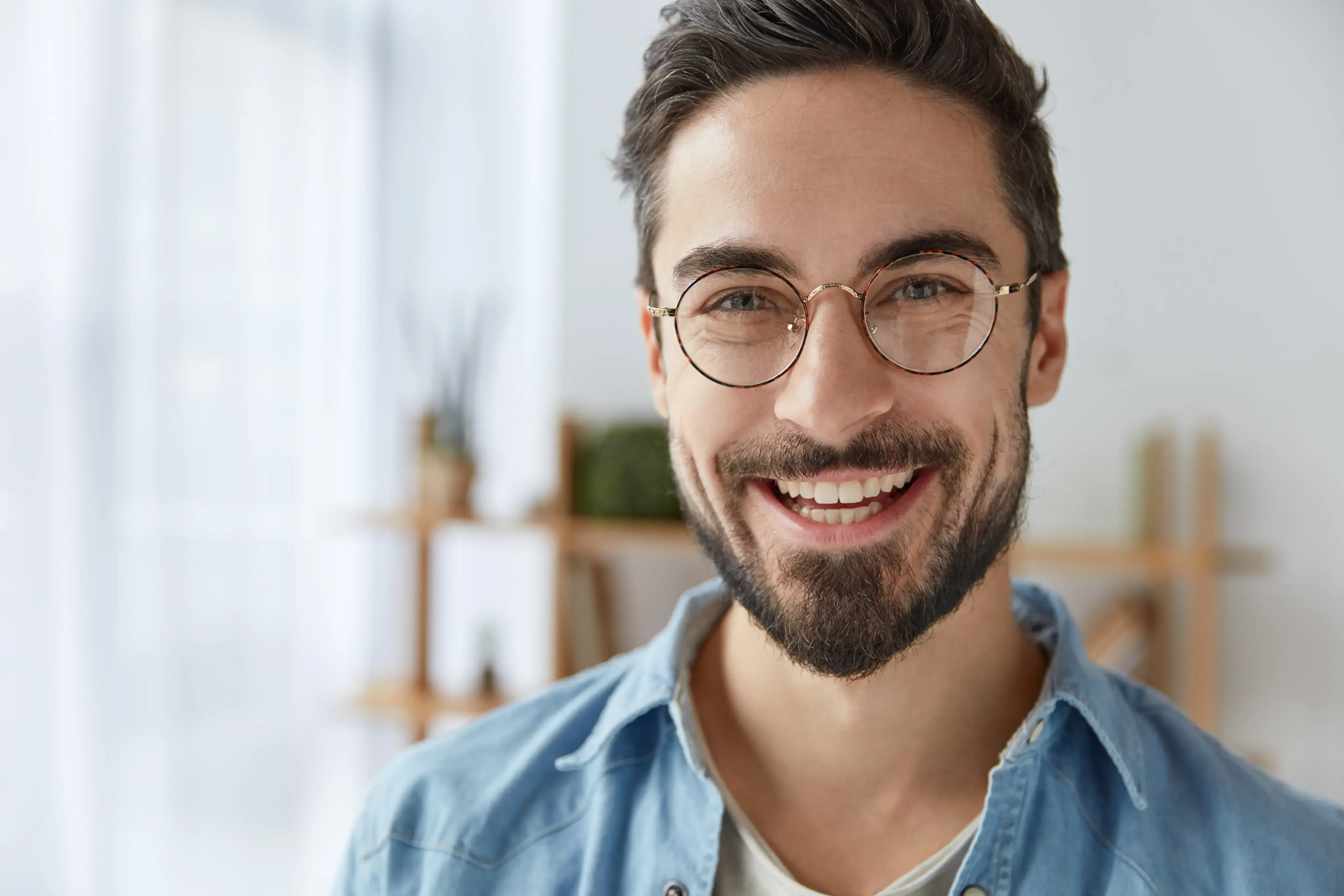 Retrato de hombre joven con barba y gafas sonriendo.