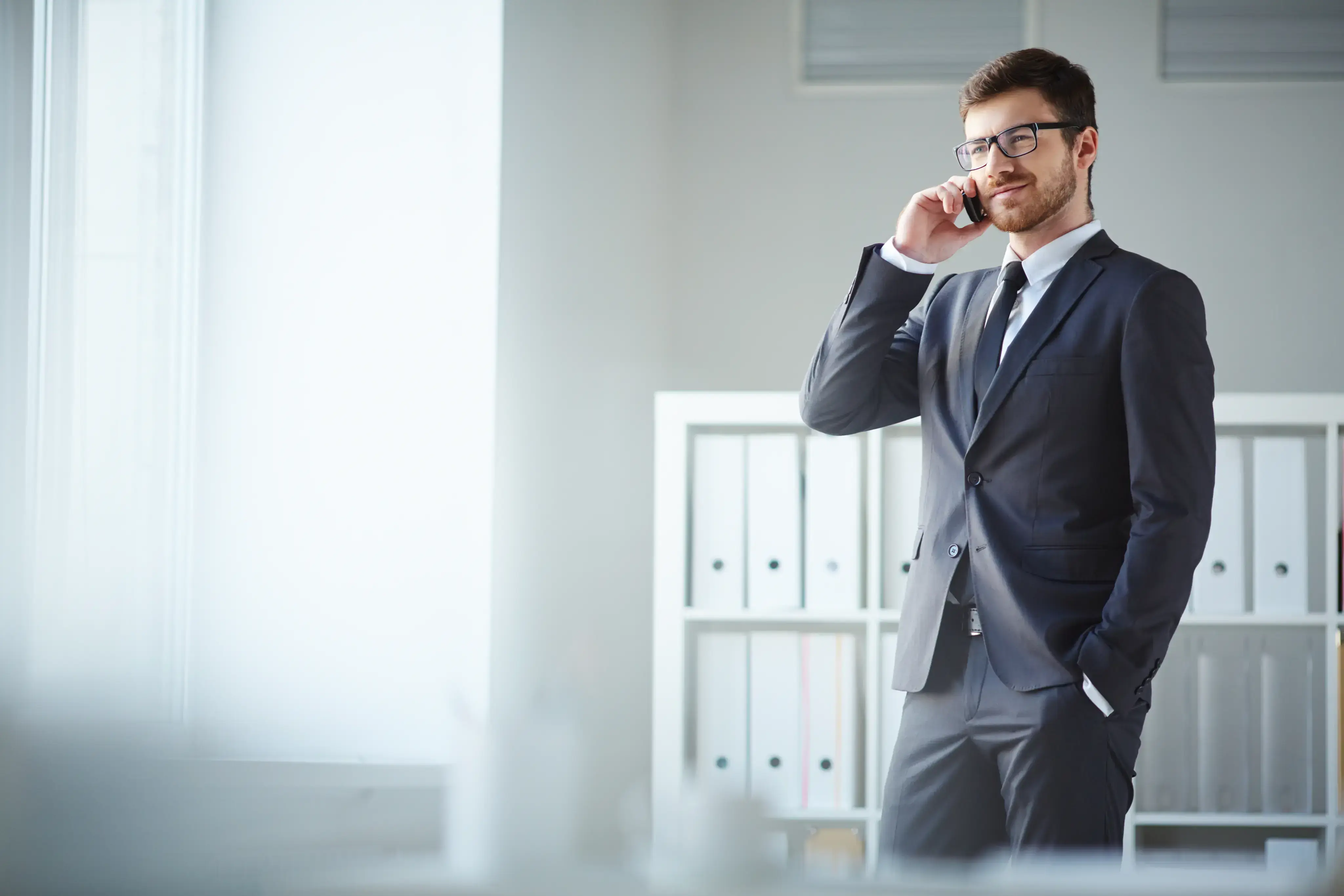 Hombre de traje hablando por teléfono en una oficina luminosa.