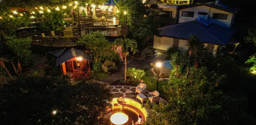 Vista nocturna del Hotel y Spa Poco a Poco con luces cálidas y área de fogata rodeada de vegetación
