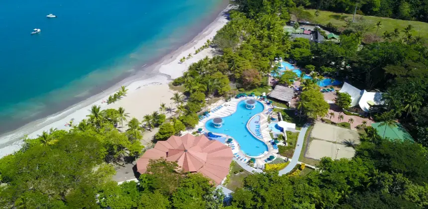 Vista aérea del Hotel Punta Leona con piscina, áreas verdes y playa de arena blanca frente al mar