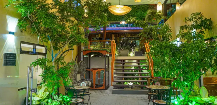 Entrada iluminada del Hotel Sibu con mesas al aire libre rodeadas de plantas y decoración tropical