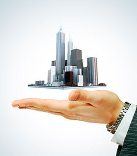 Mano extendida sosteniendo una maqueta de ciudad con varios edificios modernos.