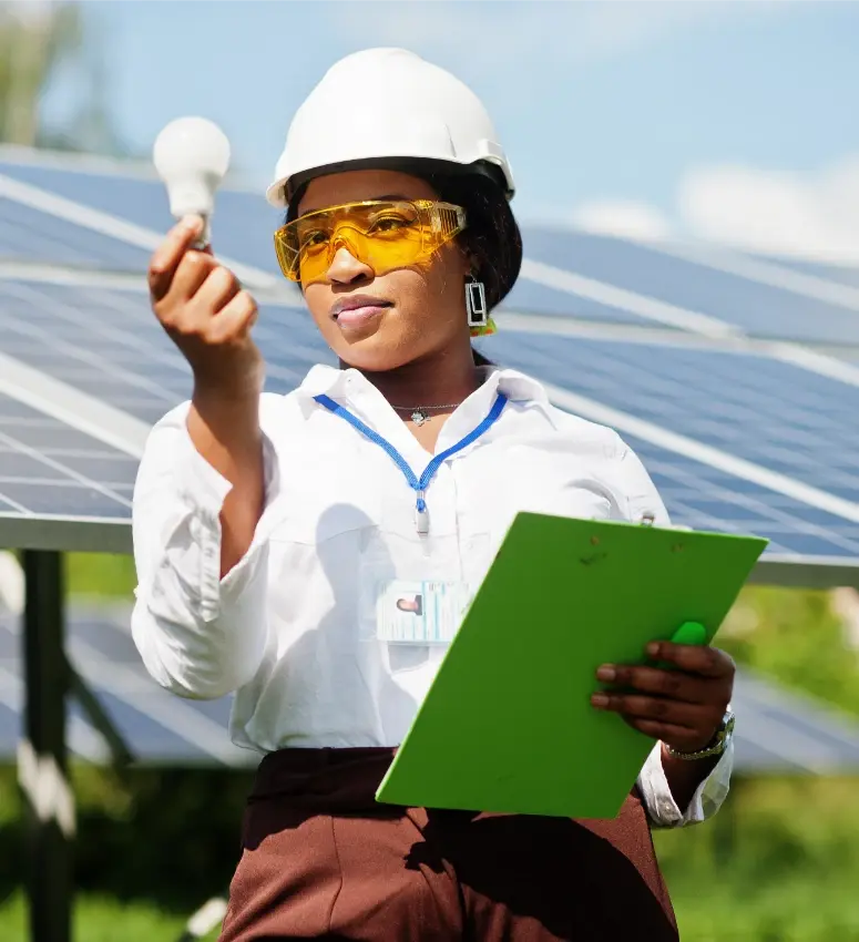 Ingeniera con casco y gafas de protección sosteniendo un foco mientras inspecciona paneles solares al aire libre.