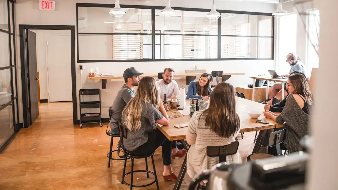 Grupo de jóvenes reunidos en un café conversando y trabajando con tabletas y laptops.