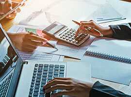 Personas usando calculadora y computadora portátil para analizar documentos financieros.