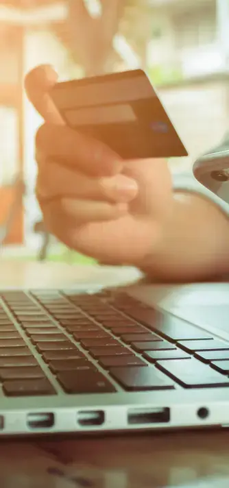 Persona sosteniendo una tarjeta de crédito frente a una computadora portátil, representando una compra en línea o transacción digital.