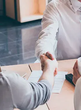 Dos personas estrechándose la mano en un escritorio de oficina.