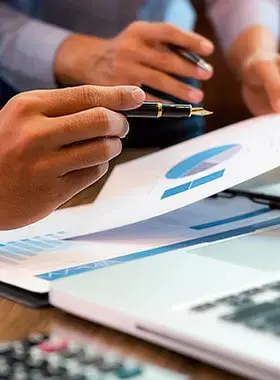 Manos señalando gráficos financieros sobre papel junto a una laptop.