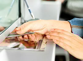 Mano entregando dinero en efectivo a través de una ventanilla de atención bancaria.