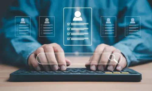 Manos escribiendo en un teclado con íconos virtuales de perfiles y barra de búsqueda flotando sobre la escena