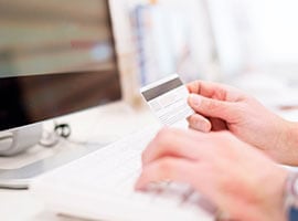 Persona sosteniendo una tarjeta de crédito frente a una computadora mientras realiza una compra en línea.